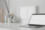 Espace de travail minimaliste et moderne avec ordinateur portable à écran blan ouvert et maquette de cadre avec décoration sur une table en bois blanc