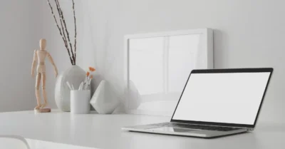 Espace de travail minimaliste et moderne avec ordinateur portable à écran blan ouvert et maquette de cadre avec décoration sur une table en bois blanc