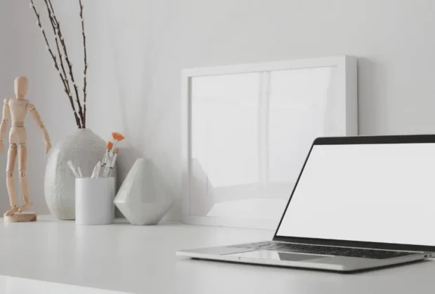 Espace de travail minimaliste et moderne avec ordinateur portable à écran blan ouvert et maquette de cadre avec décoration sur une table en bois blanc