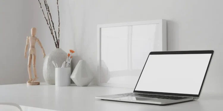 Espace de travail minimaliste et moderne avec ordinateur portable à écran blan ouvert et maquette de cadre avec décoration sur une table en bois blanc