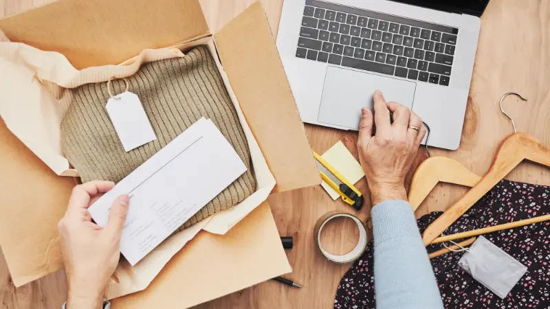 Un commerçant emballe une commande en ligne jusqu'à sa livraison. Il prépare un colis contenant des vêtement de la boutique en ligne