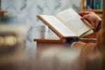 Des mains d'un homme entrain de lire un livre de développement personnel sur un bureau
