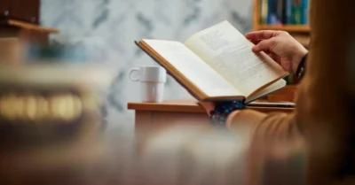 Des mains d'un homme entrain de lire un livre de développement personnel sur un bureau