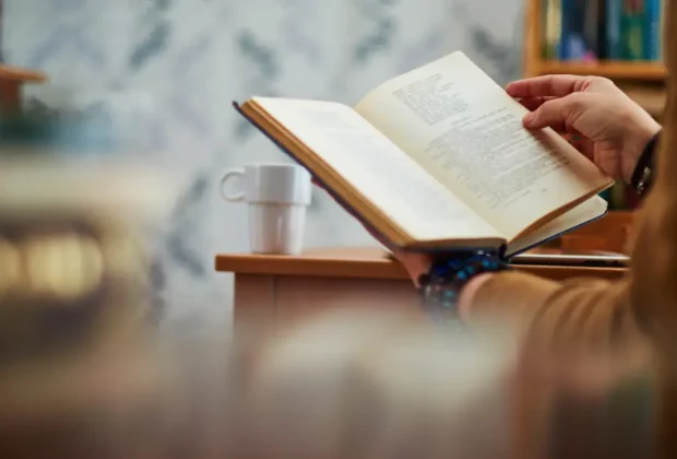 Des mains d'un homme entrain de lire un livre de développement personnel sur un bureau
