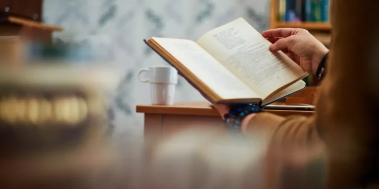 Des mains d'un homme entrain de lire un livre de développement personnel sur un bureau