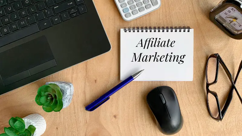 Mots de marketing d'affiliation sur un carnet. avec stylo, souris, calculatrice, plante, ordinteur portable et fond de table marron